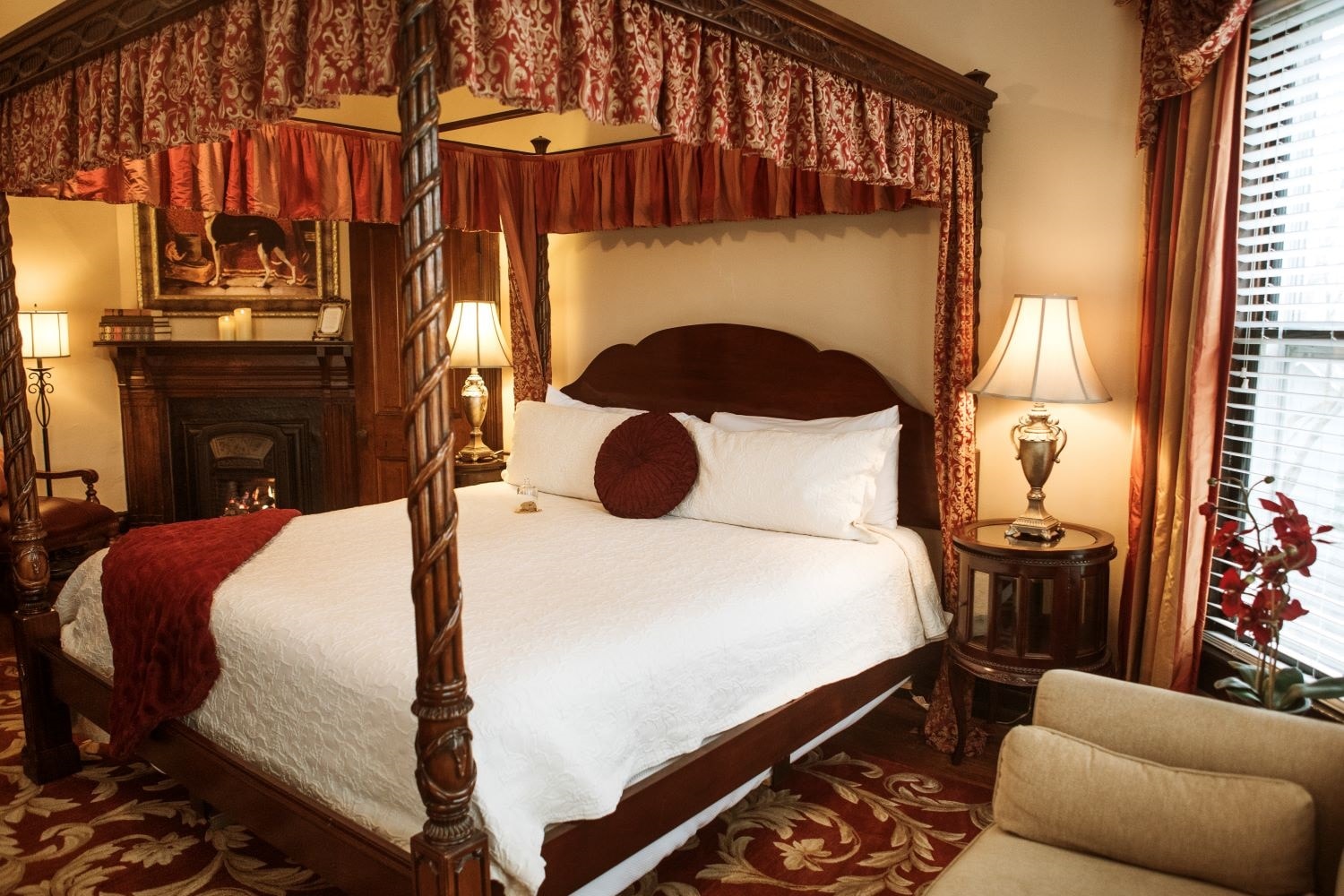 A luxurious four-poster bed in a warmly decorated bedroom with a fireplace and elegant furnishings.