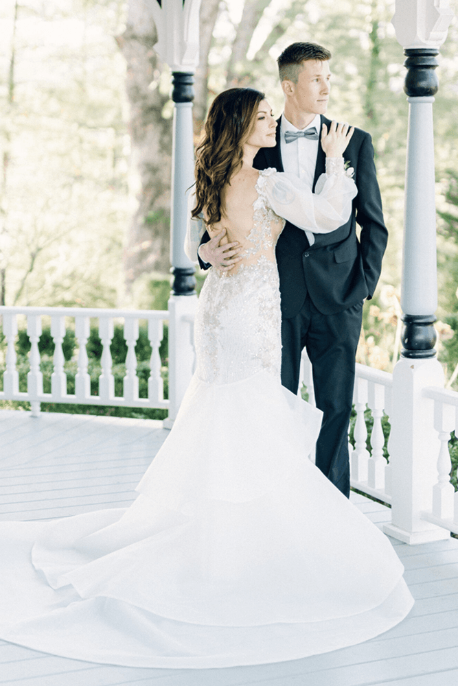 A bride and groom embrace on a picturesque porch, showcasing elegant wedding attire.