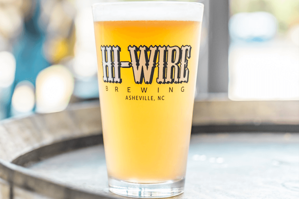 Pint glass of Hi-Wire Brewing beer on a wooden surface.
