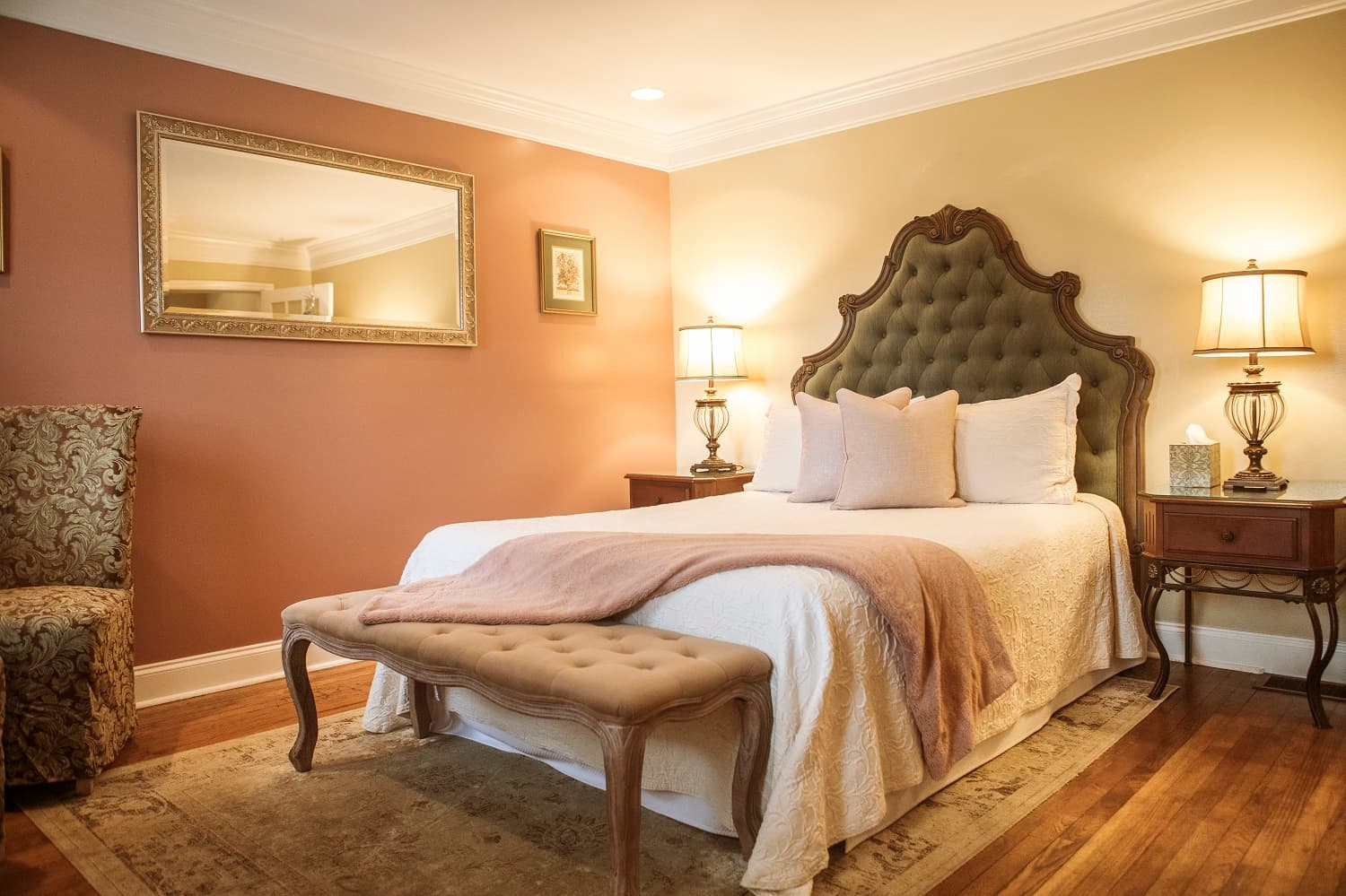 A cozy bedroom featuring a tufted headboard, elegant lamps, and warm pastel walls.
