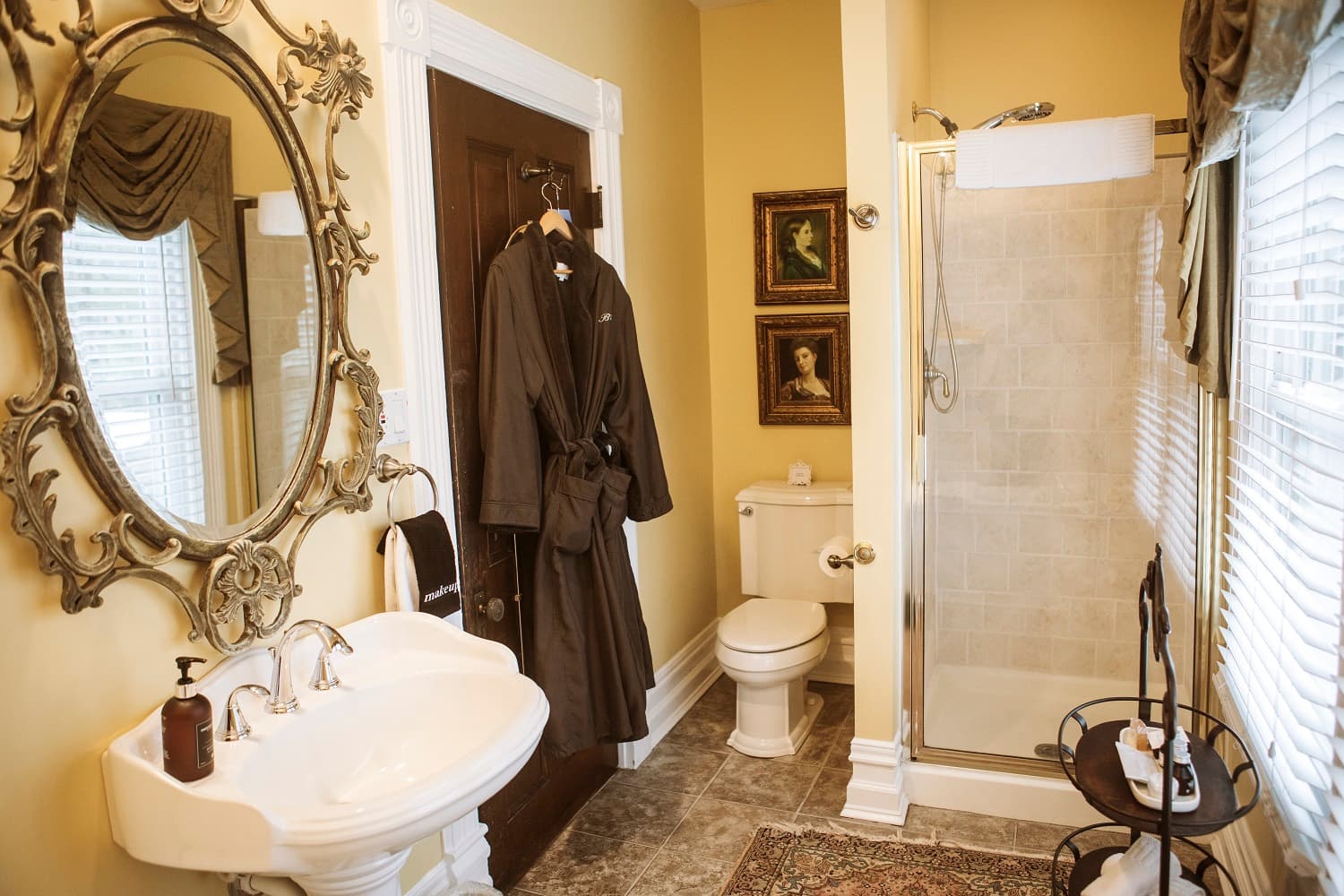 A well-decorated bathroom featuring a vintage mirror, a plush robe hanging on the door, and a glass shower.