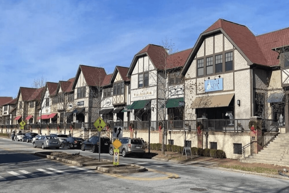 A row of charming shops with gabled roofs and festive decorations along a sunny street.