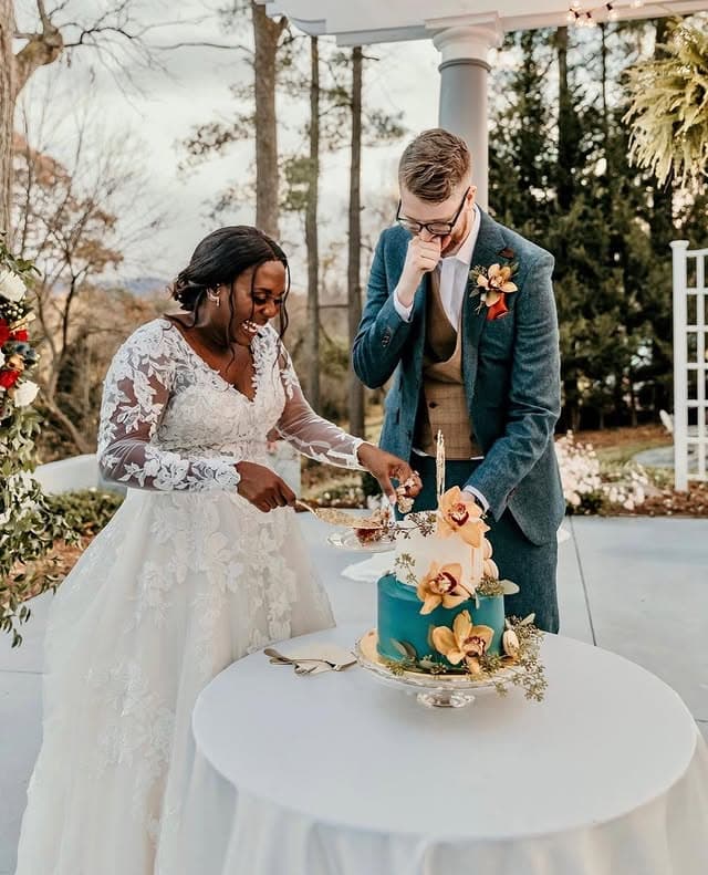 A bride and groom cut their wedding cake together outdoors.