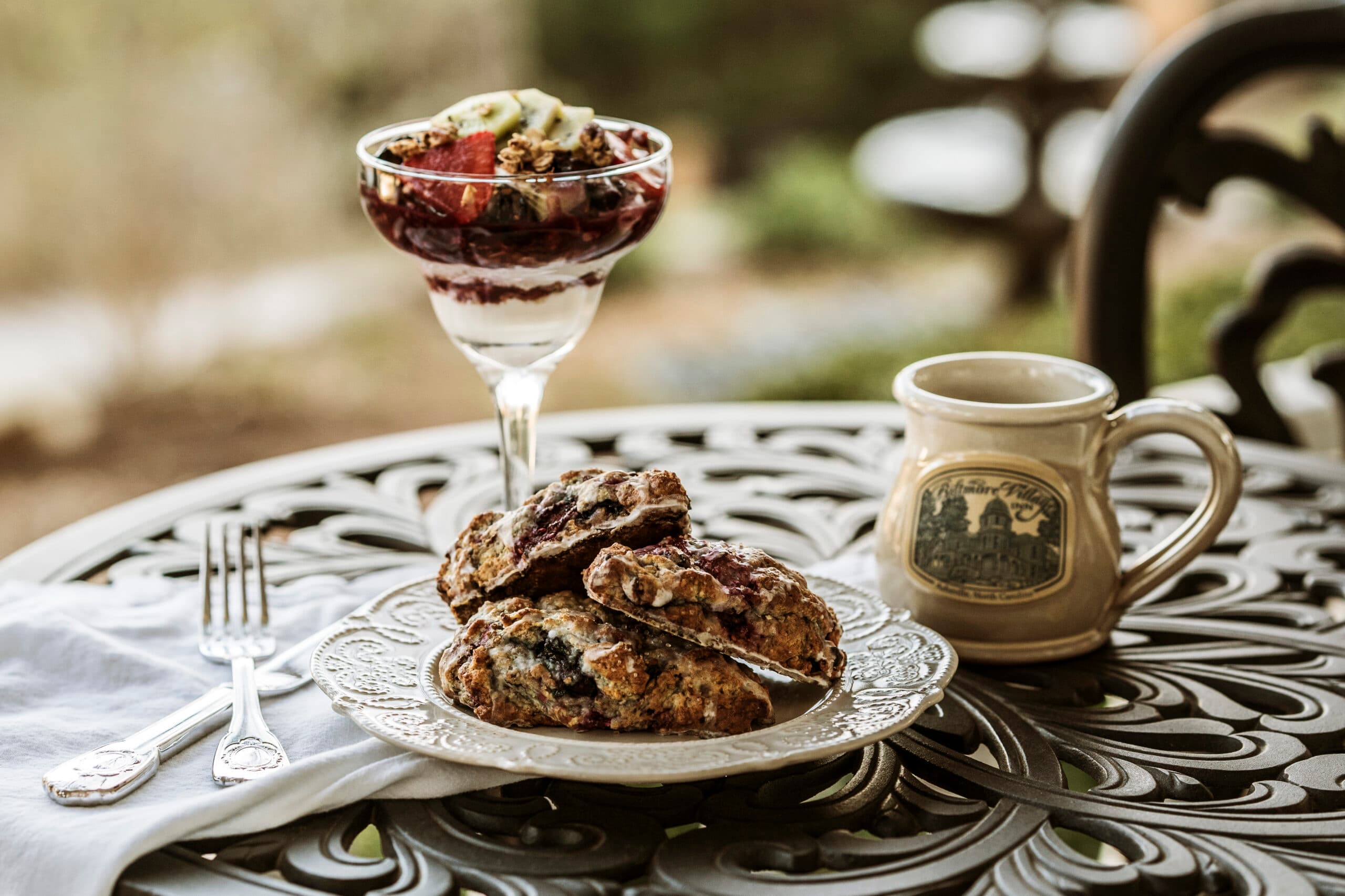A plate of fresh biscuits, a parfait, and a mug on an ornate table.