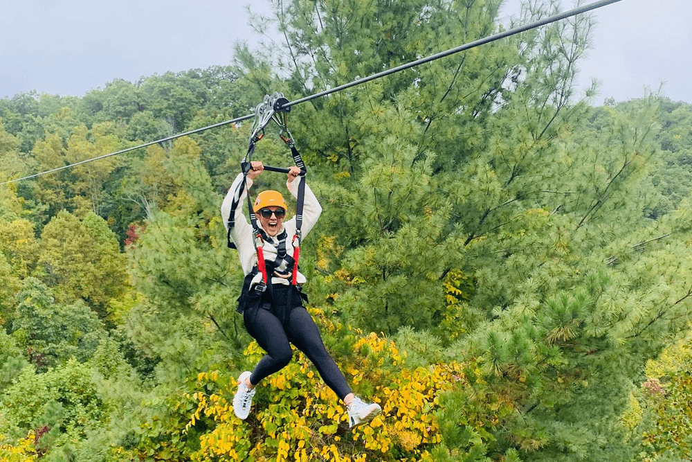 A person excitedly zips along a zip line above colorful autumn trees.