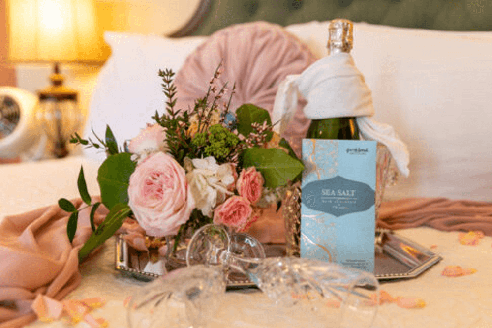 A bottle of "Sea Salt" sparkling beverage next to a bouquet of roses on a bed with soft linens.