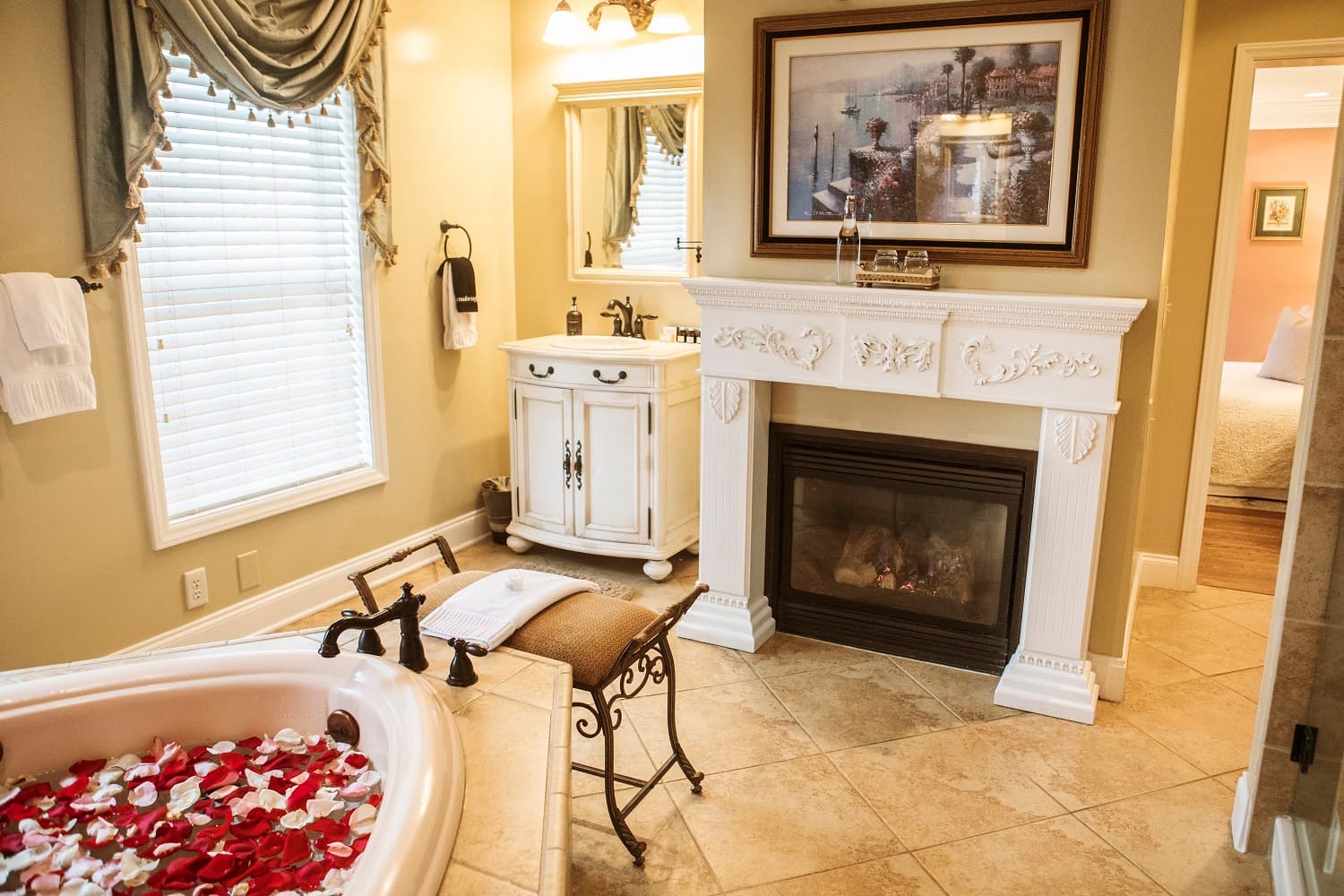 A luxurious bathroom featuring a rose petal-filled bathtub, elegant decor, and a cozy fireplace.