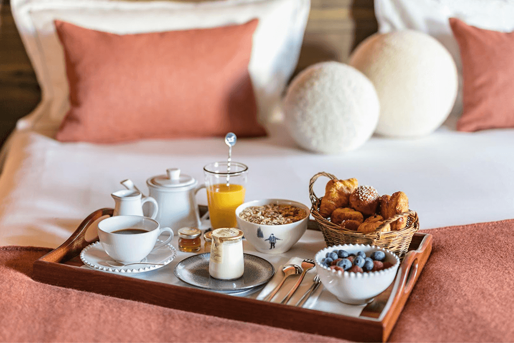 A breakfast tray with coffee, orange juice, cereal, pastries, and fresh berries on a neatly made bed.