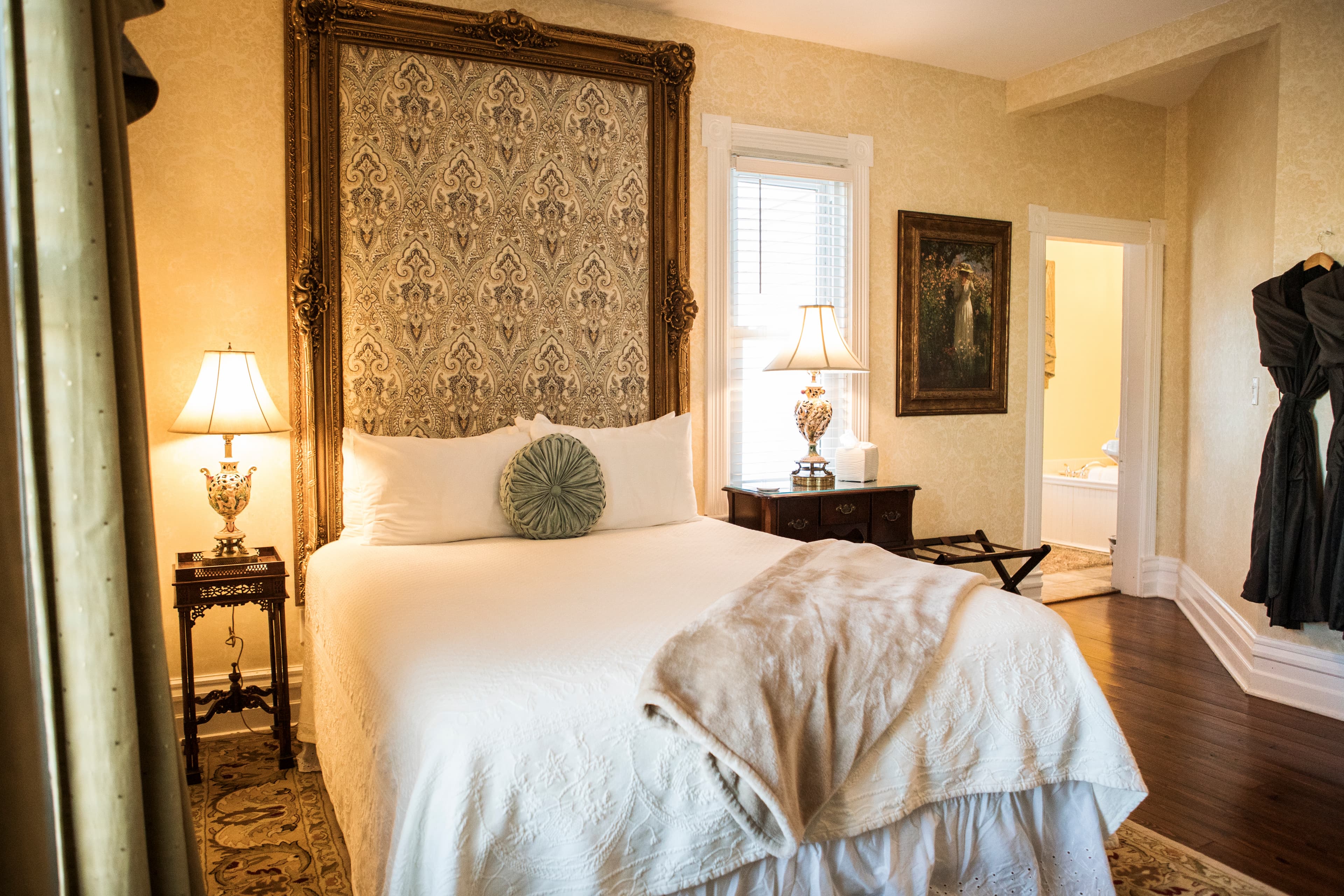 A cozy bedroom featuring a large bed with decorative pillows, elegant lamps, and a vintage touch.