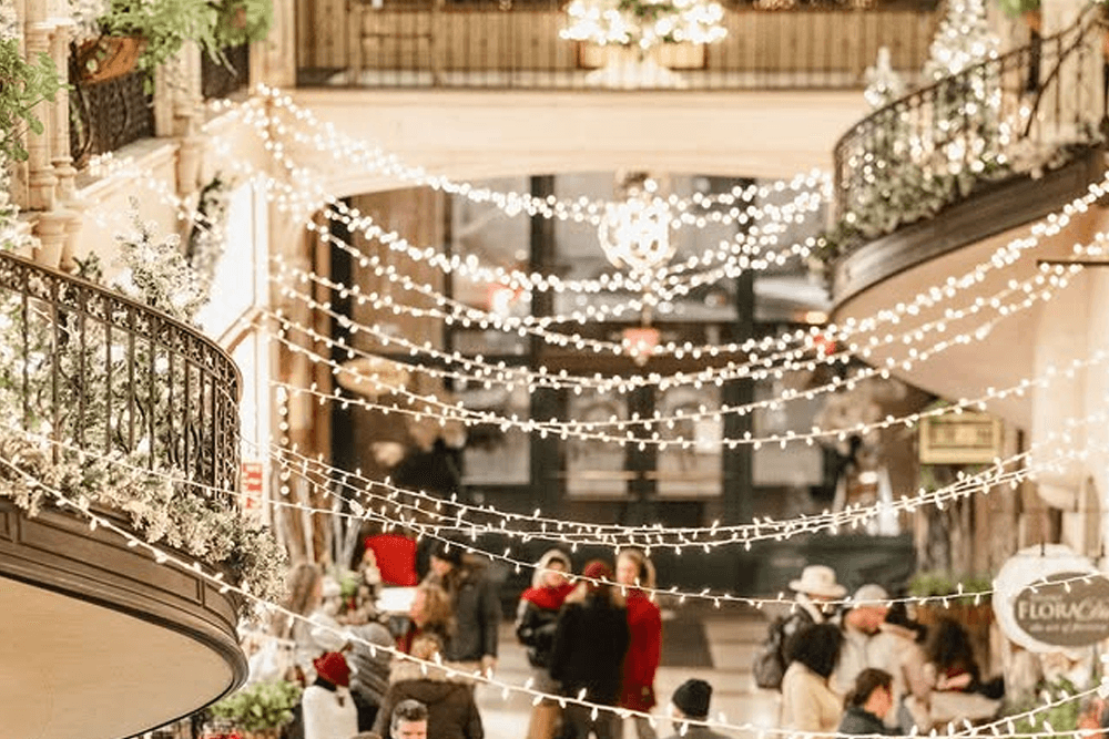 A bustling indoor space adorned with twinkling holiday lights and greenery.