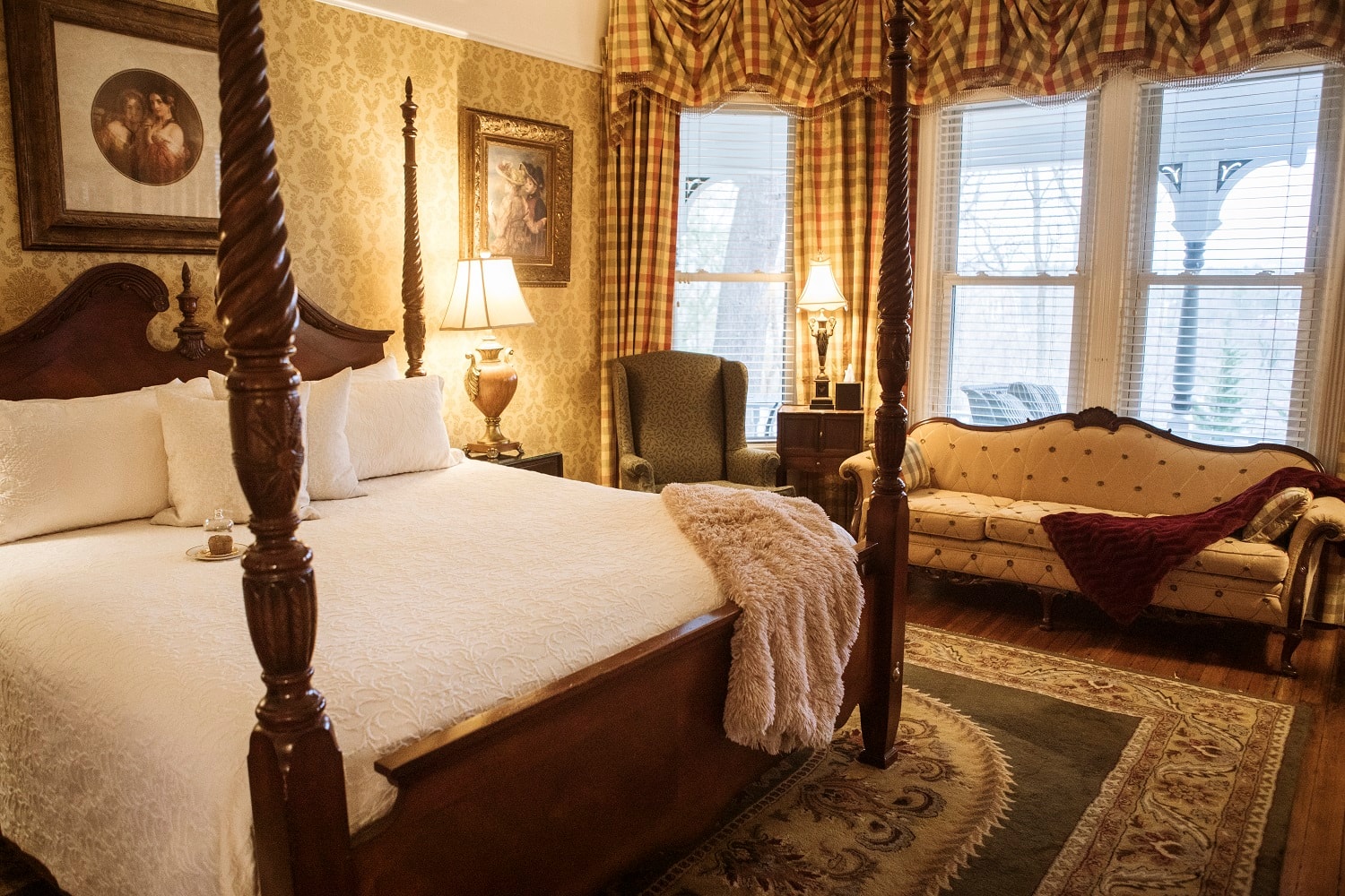A cozy bedroom featuring a four-poster bed, elegant furnishings, and soft natural light from the windows.
