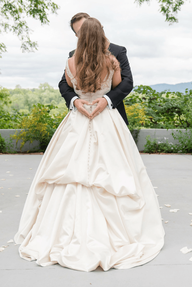 A couple embraces, with the groom forming a heart shape with his hands behind the bride's back.