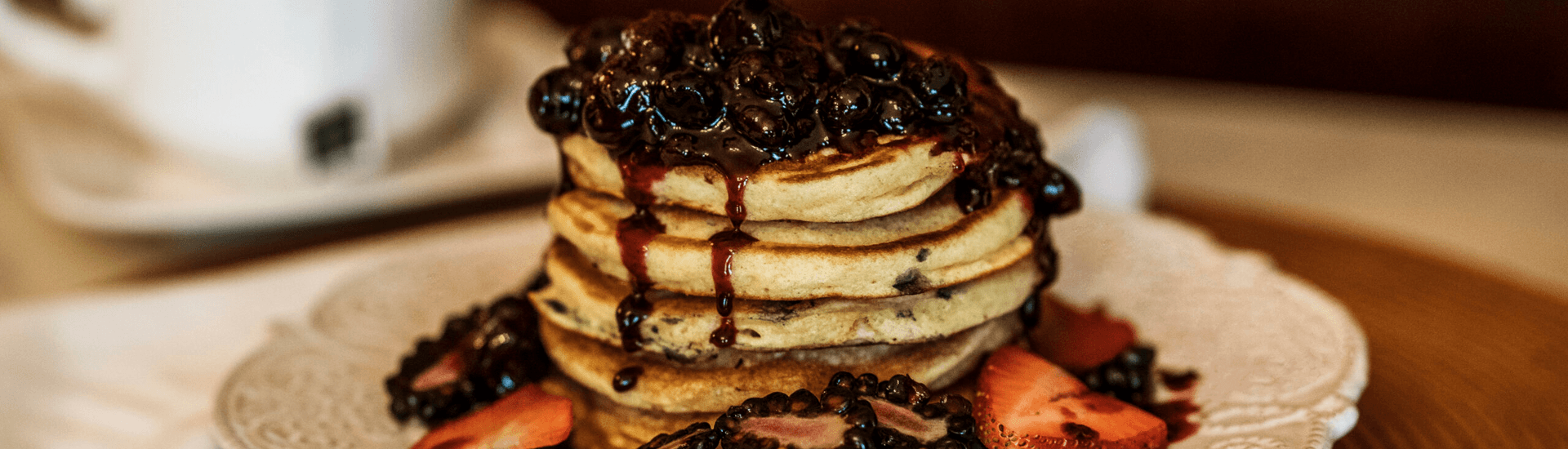 Stack of pancakes topped with berries and syrup, surrounded by sliced strawberries.
