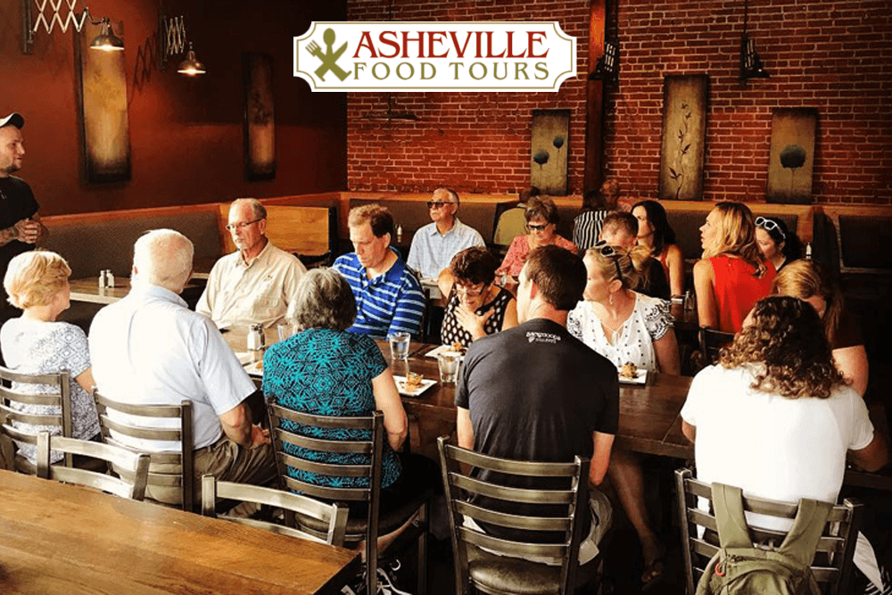 A diverse group of people seated at a long table in a restaurant during a food tour in Asheville.