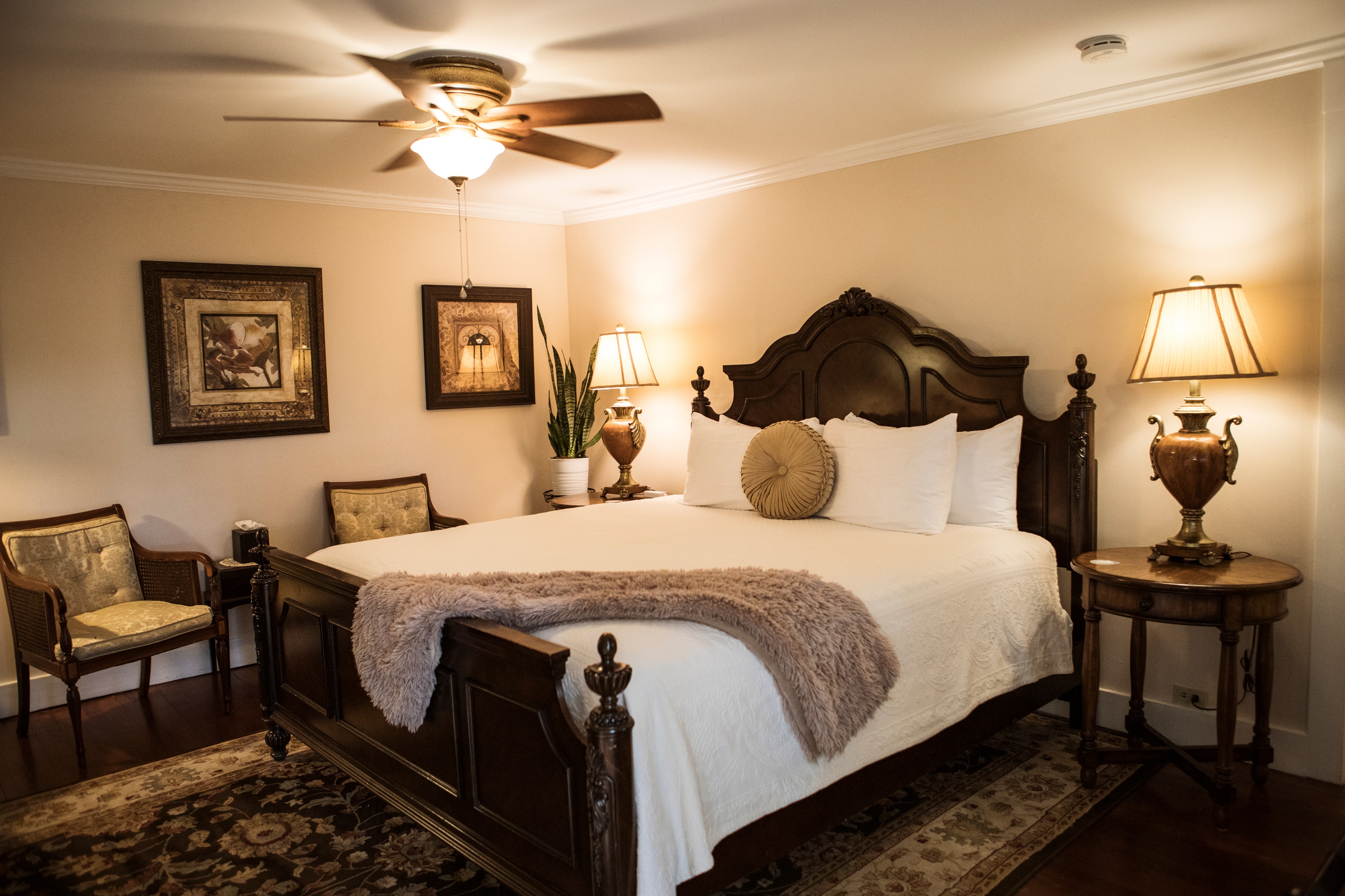 A cozy bedroom featuring a wooden bed, two lamps, and decorative artwork.
