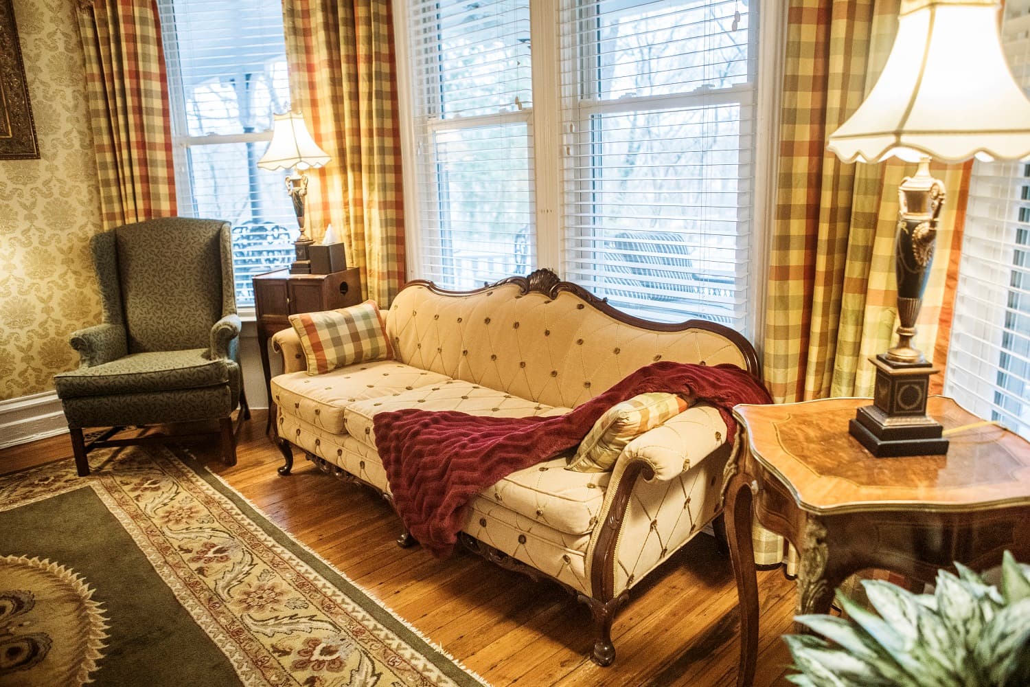 A cozy living room featuring an elegant sofa with a deep red throw, a patterned rug, and warm lamp lighting.
