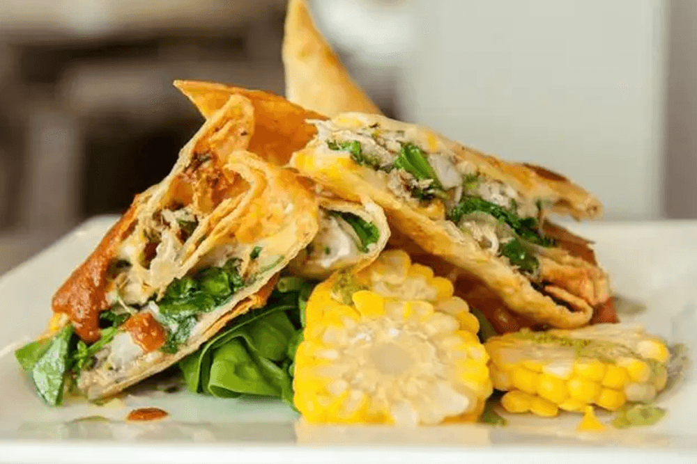 A plate of crispy tortillas filled with chicken and greens, served with corn and salsa.