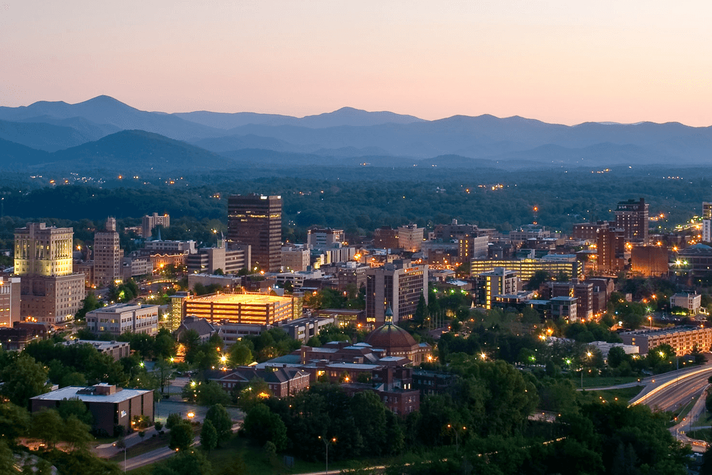 A panoramic view of a city skyline against a backdrop of mountains at dusk.
