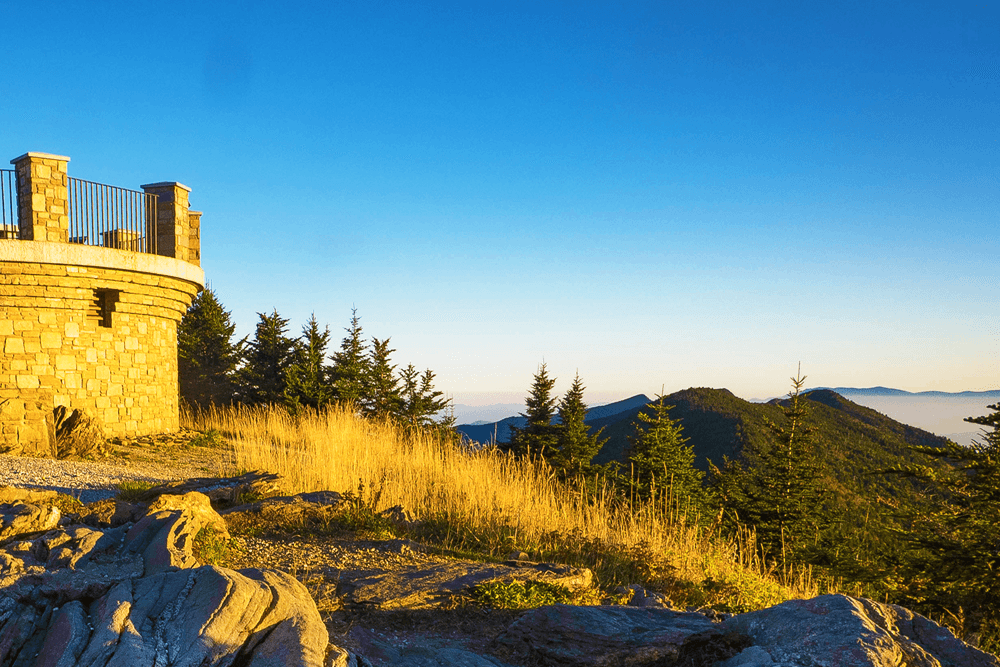 A stone observation tower overlooks rolling mountains under a clear blue sky.