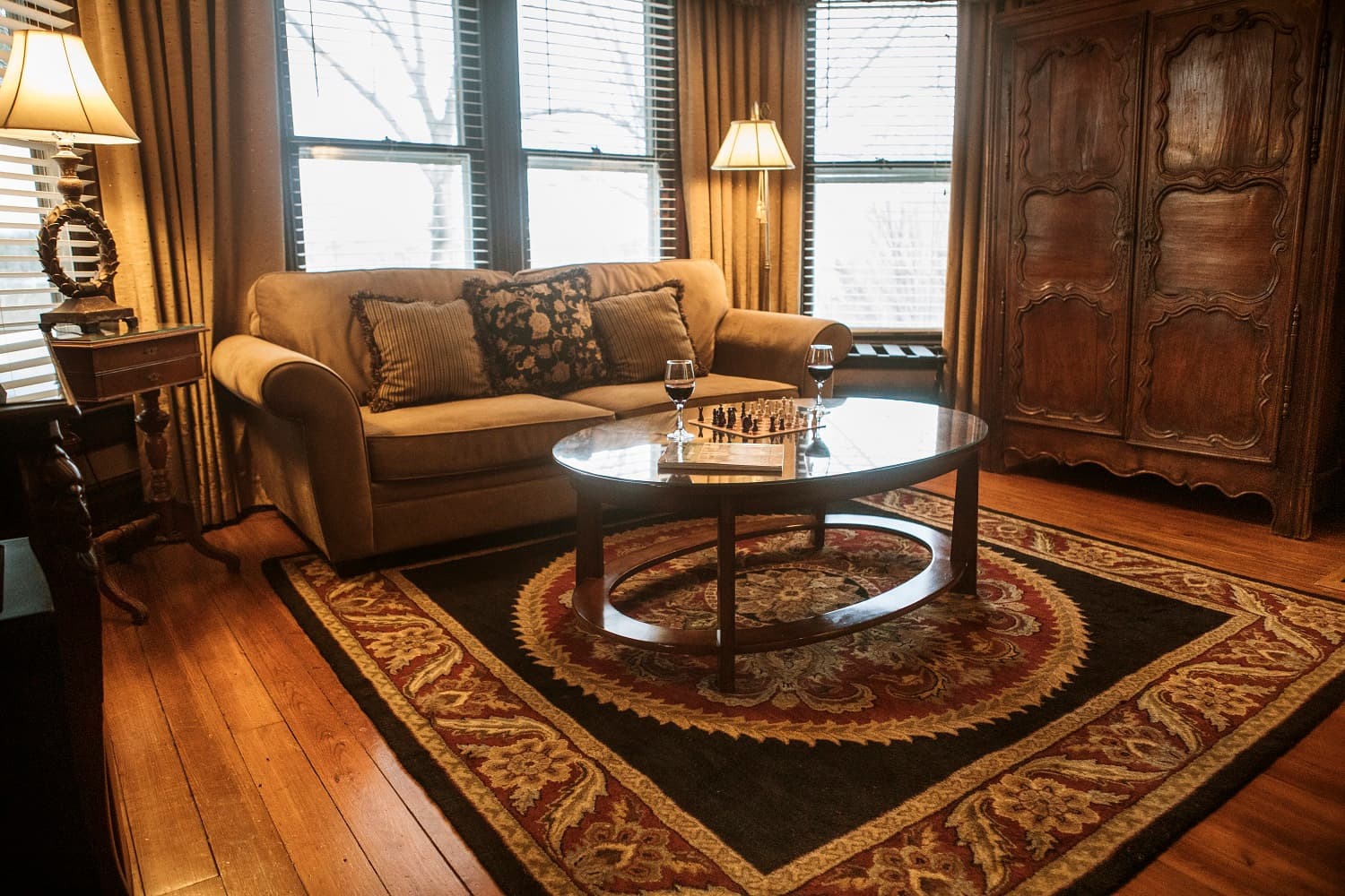 A cozy living room featuring a sofa, a coffee table with wine glasses, and large windows.