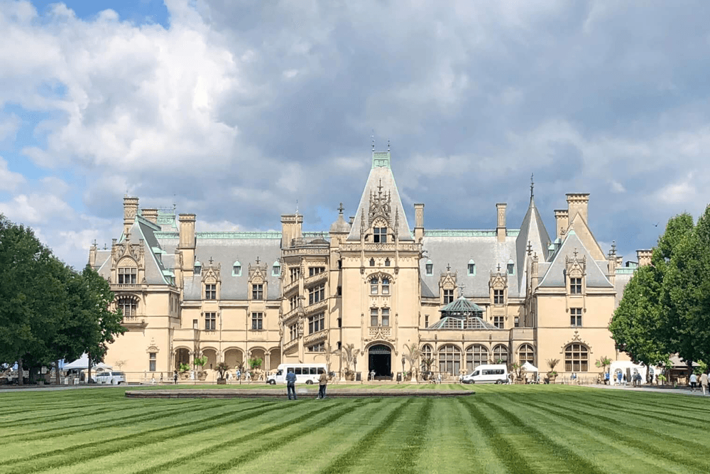 A grand mansion with a lush green lawn and cloudy sky in the background.