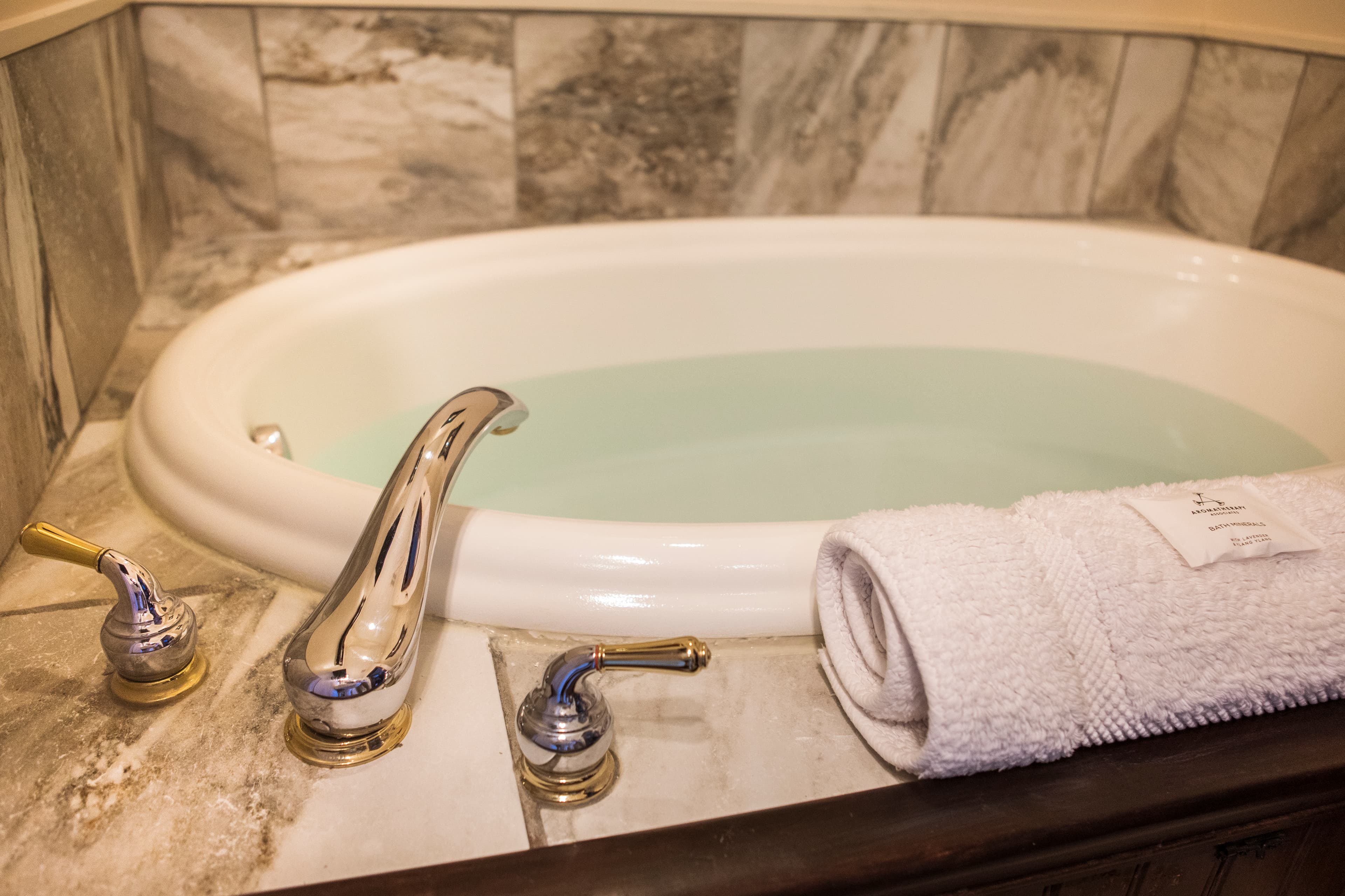 A luxurious bathtub with water and a neatly rolled white towel beside it.