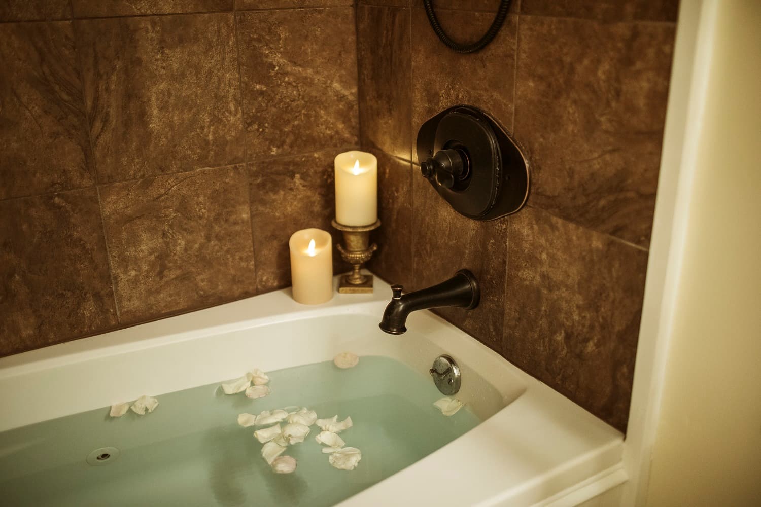 A serene bathtub filled with water and floating rose petals, accompanied by lit candles.