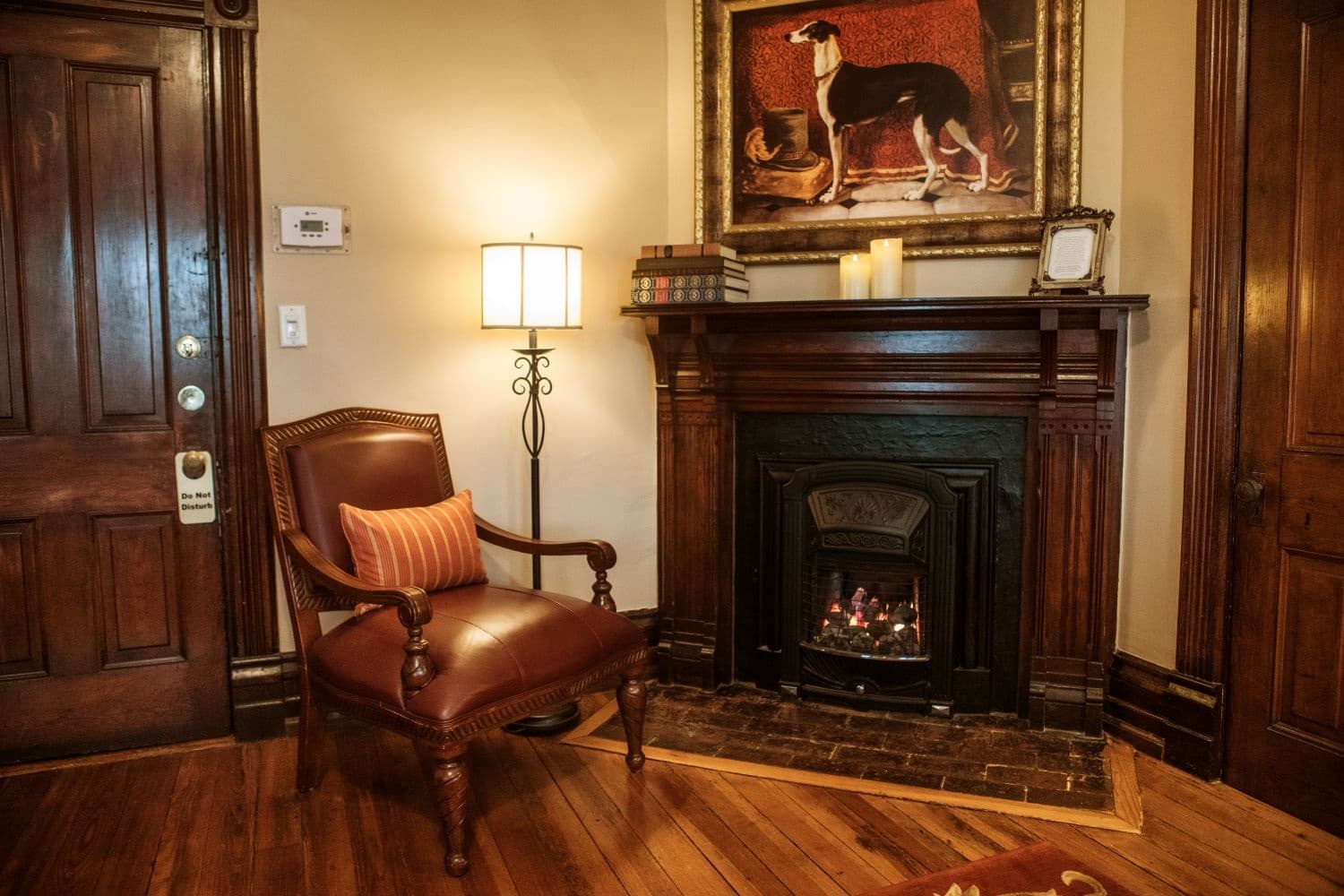 A cozy corner featuring a leather armchair, a warm fireplace, and a framed dog painting.