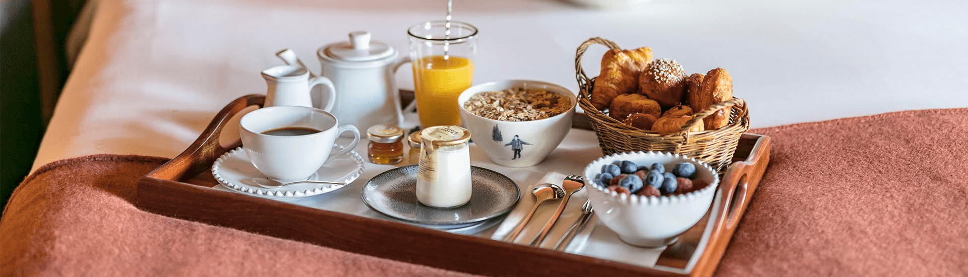 A breakfast tray featuring coffee, orange juice, yogurt, granola, pastries, and berries.