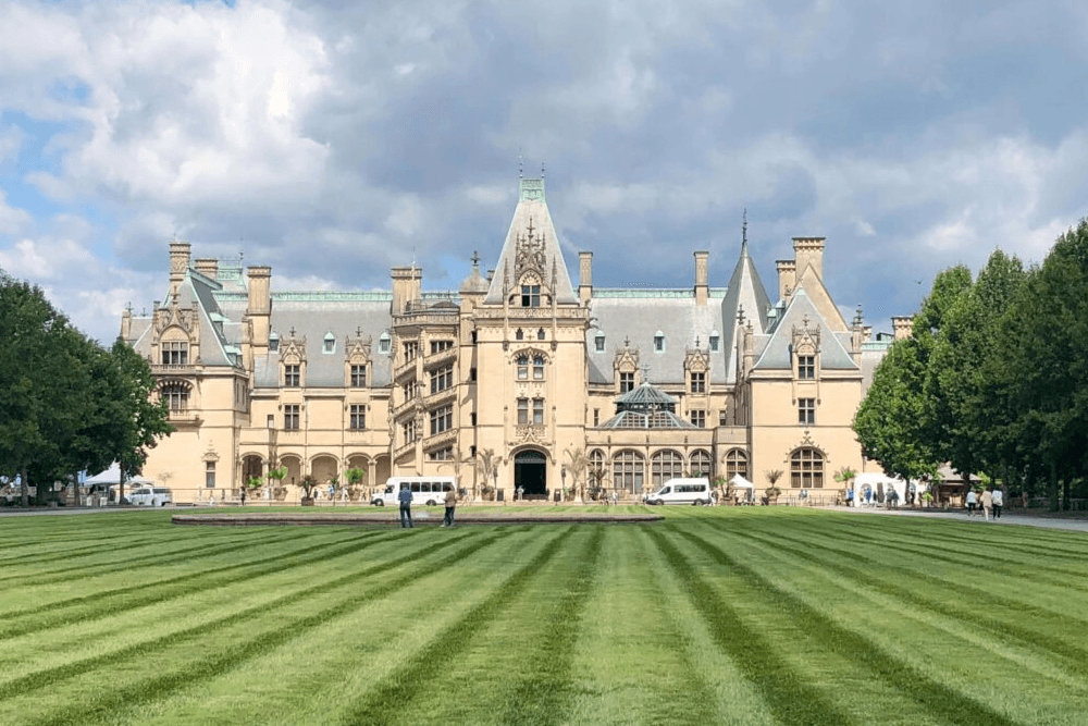 A majestic mansion surrounded by neatly manicured lawns and trees under a partly cloudy sky.