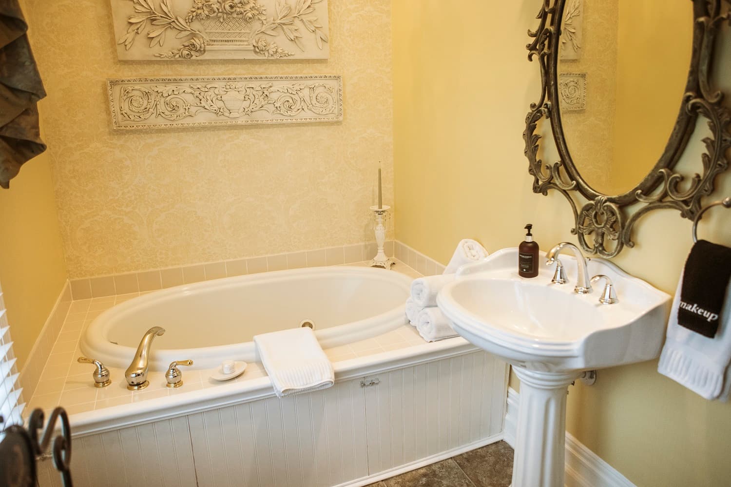 A luxurious bathroom featuring a jacuzzi tub, elegant sink, and decorative mirror against soft yellow walls.