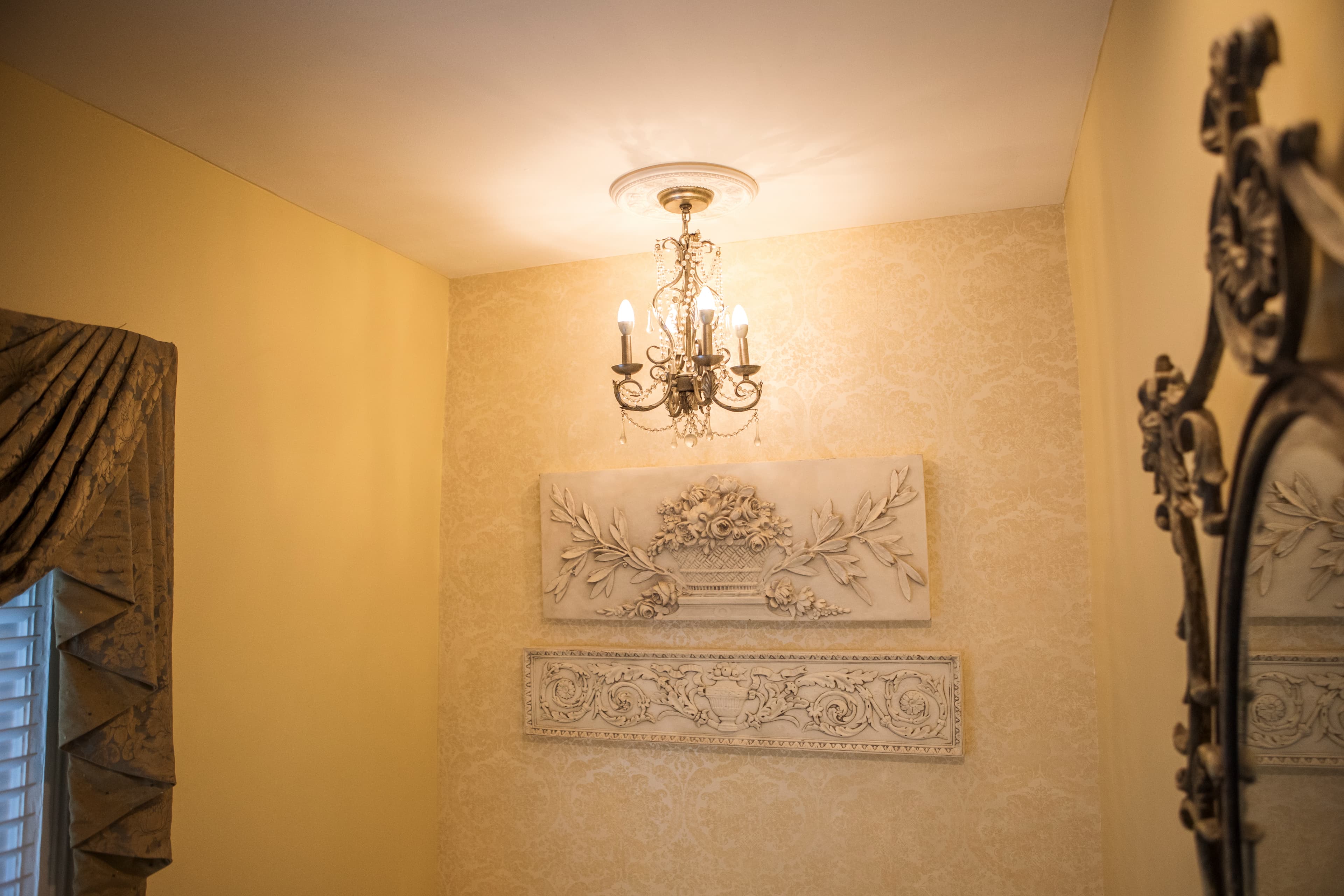 A cozy corner with a decorative chandelier, textured wall art, and soft golden walls.