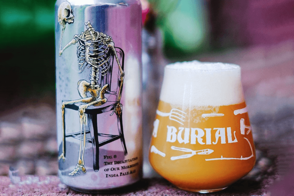 A can of beer featuring a skeleton sitting on a chair next to a frothy glass of pale ale.